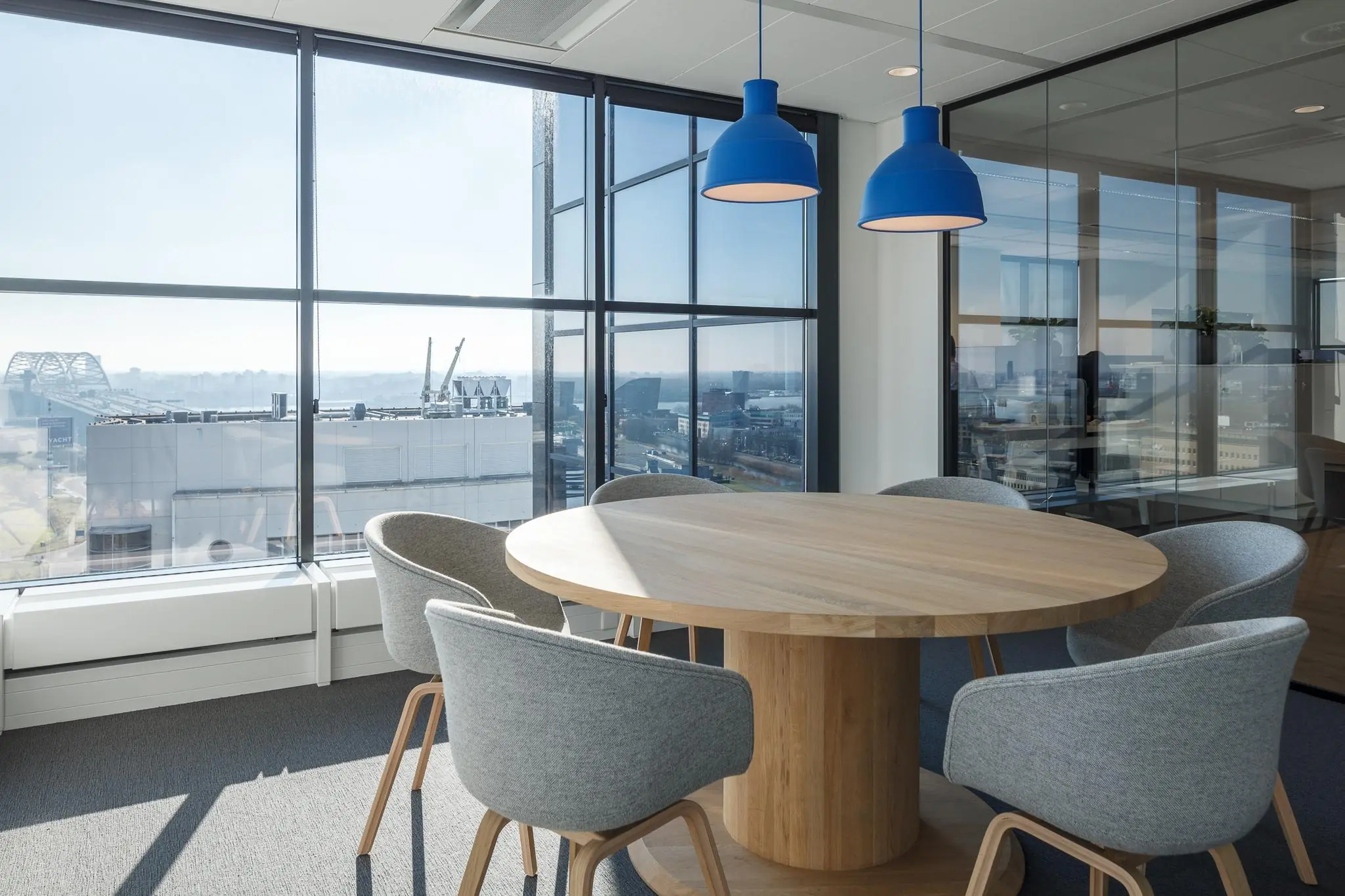 Vergaderruimte met ronde houten tafel, grijze stoelen en uitzicht op Rivium Quadrant in Rotterdam.